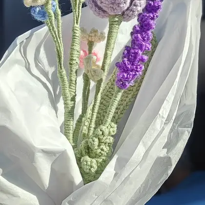 A crocheted bouquet of purple tulips, lavender sprigs and small white and pink flowers wrapped in white paper
