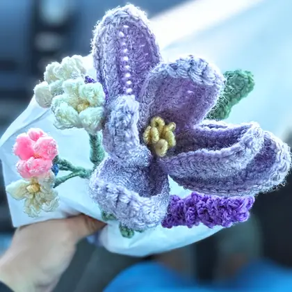 A crocheted bouquet of purple tulips, lavender sprigs and small white and pink flowers wrapped in white paper