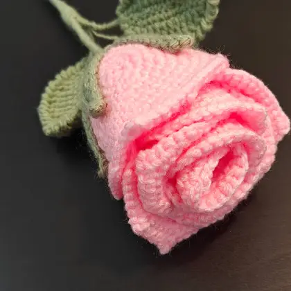 A crocheted bouquet with a large pink rose, red strawberries and green leaves wrapped in pink paper
