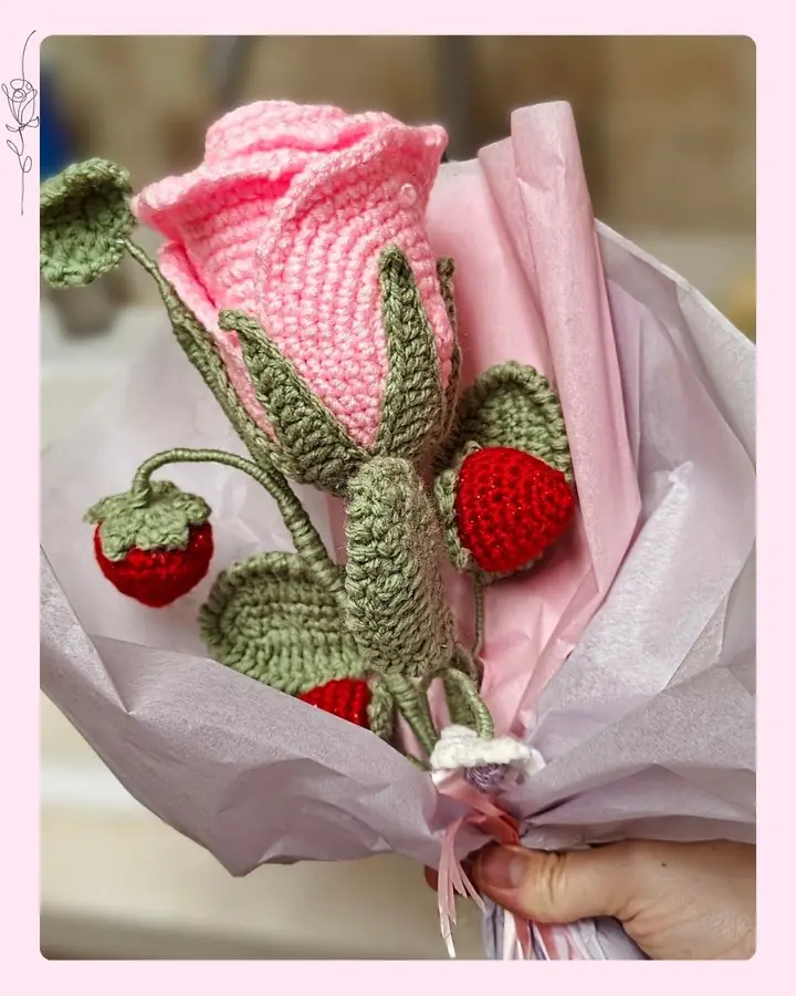 A crocheted pink rose with wired petals and a wooden stem