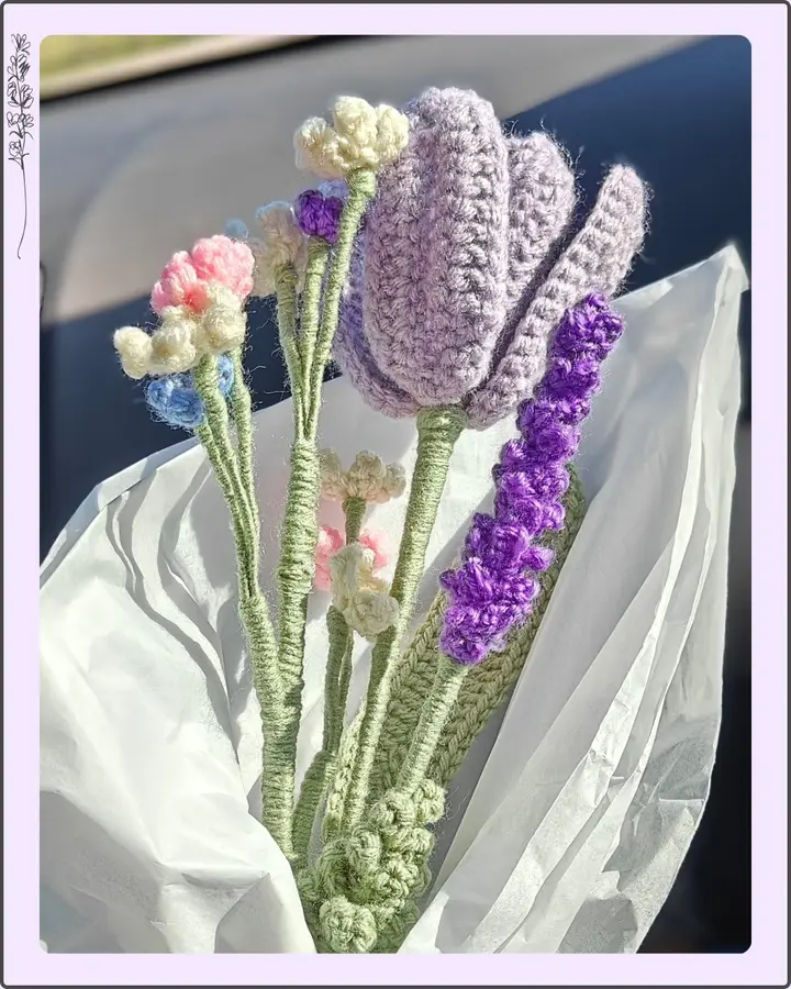 A crocheted bouquet of purple tulips, lavender sprigs and small white and pink flowers wrapped in white paper