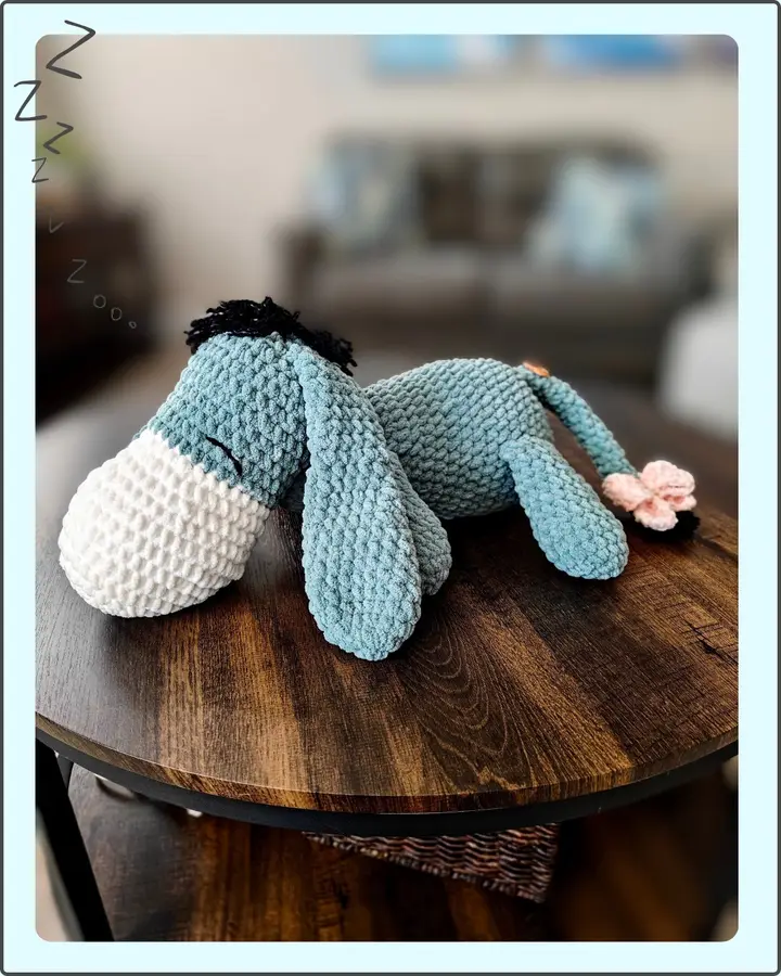 A crocheted Eeyore in soft grey with a pink muzzle and pale pink bow on his tail
